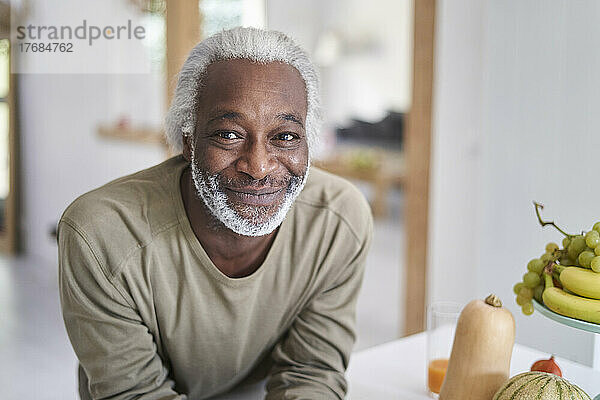 Lächelnder älterer Mann lehnt an Küchenarbeitsplatte
