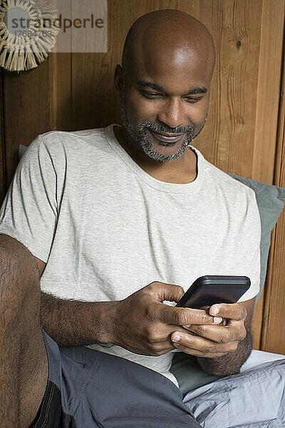 Mann benutzt Smartphone  während er im Schlafzimmer sitzt