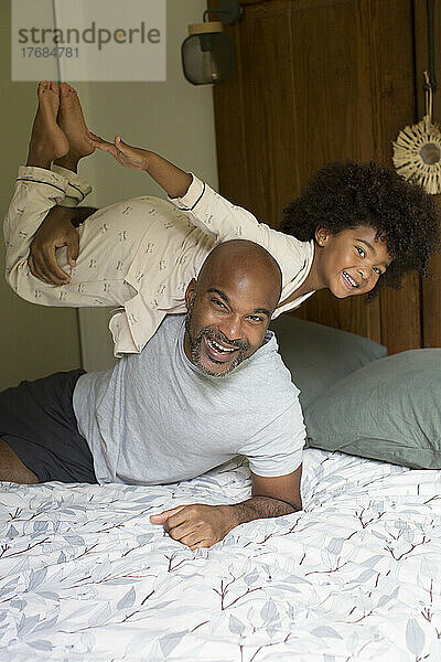 Lächelnder Vater trägt seine Tochter im Schlafzimmer auf der Schulter