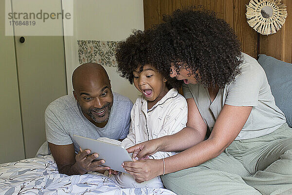 Eltern mit Tochter nutzen digitales Tablet im Schlafzimmer