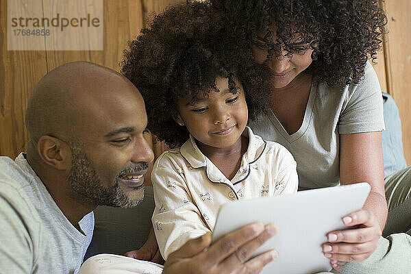 Eltern mit Tochter nutzen digitales Tablet im Schlafzimmer