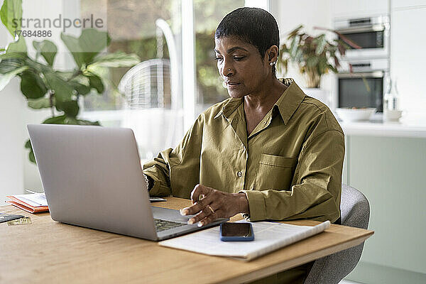 Reife Frau hält Smartphone in der Hand und benutzt Laptop