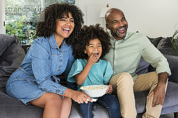 Glückliche Familie  die gemeinsam fernsieht  während sie auf dem Sofa sitzt