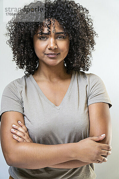 Woman with arms crossed standing against white wall