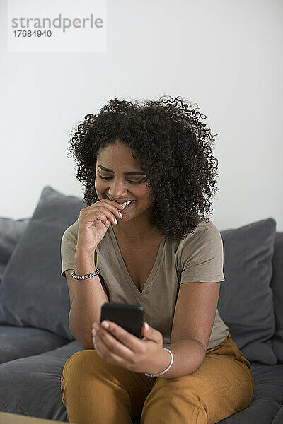 Frau benutzt Smartphone  während sie auf dem Sofa sitzt