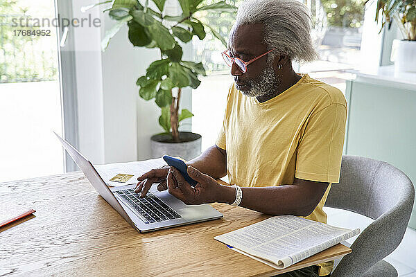 Älterer Mann benutzt Smartphone und Laptop