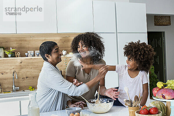 Mehrgenerationenfamilie streut Mehl in der Küche  während sie Kekse zubereitet
