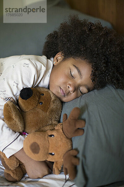 Mädchen schläft mit Spielzeug auf dem Bett