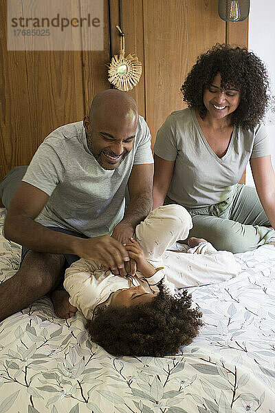 Happy parents playing with daughter on bed