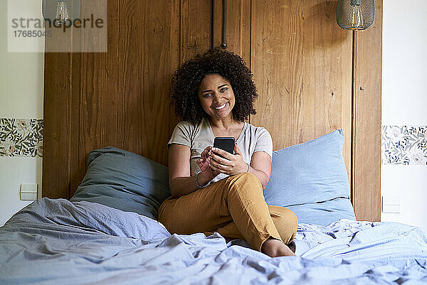 Frau benutzt Smartphone  während sie im Schlafzimmer sitzt