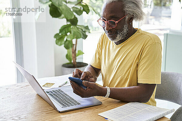 Älterer Mann benutzt Smartphone und Laptop