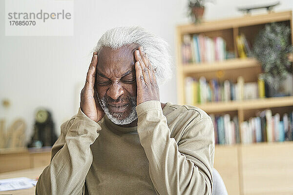 Älterer Mann leidet unter Kopfschmerzen  während er im Wohnzimmer sitzt