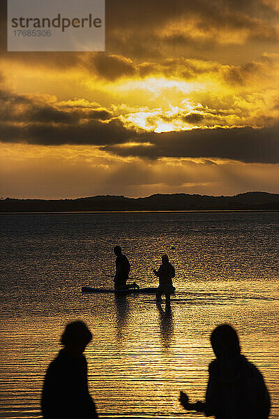 Silhouetted Familie mit Paddleboard im Meer unter dramatischen Himmel bei Sonnenuntergang
