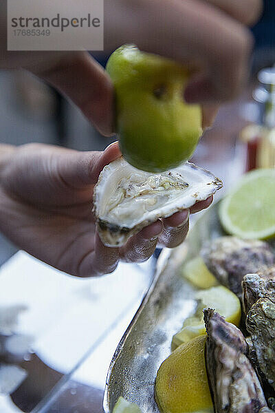 Nahaufnahme: Hand drückt Limette über frische Auster