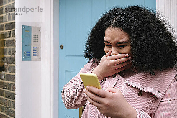 Junge Frau mit Hand vor Mund und Mobiltelefon