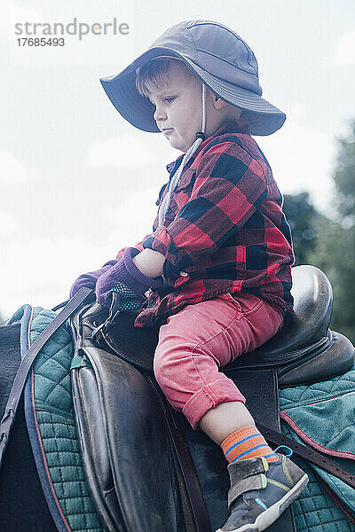 Junge mit Hut sitzt auf einem Pferd