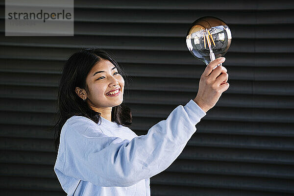Smiling young woman holding light bulb