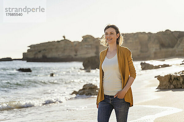 Lächelnde Frau  die an einem sonnigen Tag am Strand spaziert
