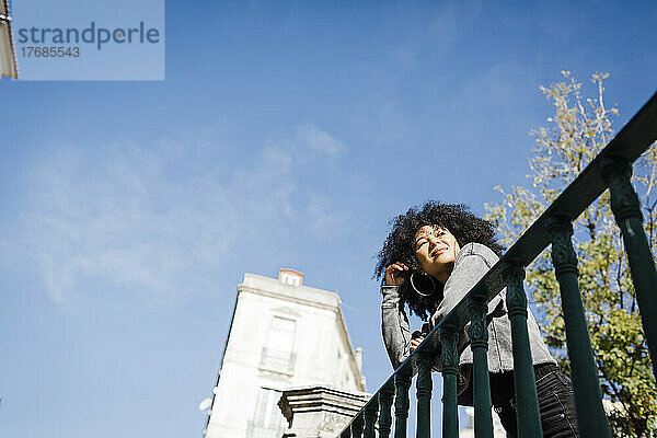 Lächelnde Frau  die an einem sonnigen Tag am Geländer steht