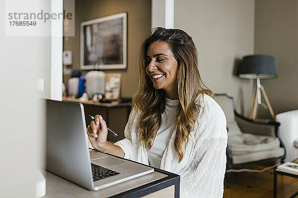 Lächelnde Geschäftsfrau  die zu Hause einen Videoanruf über ihren Laptop tätigt
