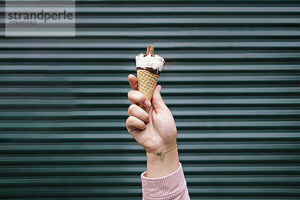 Hand of woman holding holding ice cream in front of shutter
