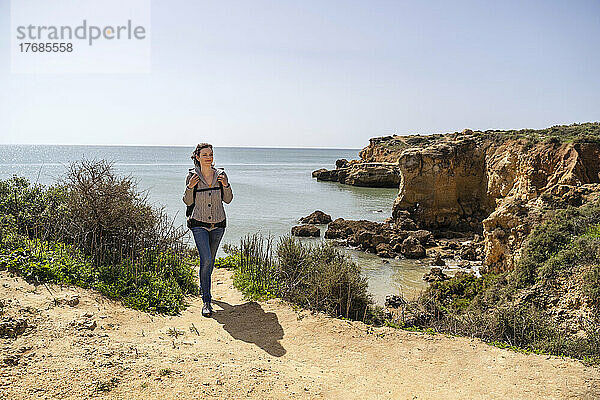 Frau geht mit Rucksack auf Klippe vor dem Meer