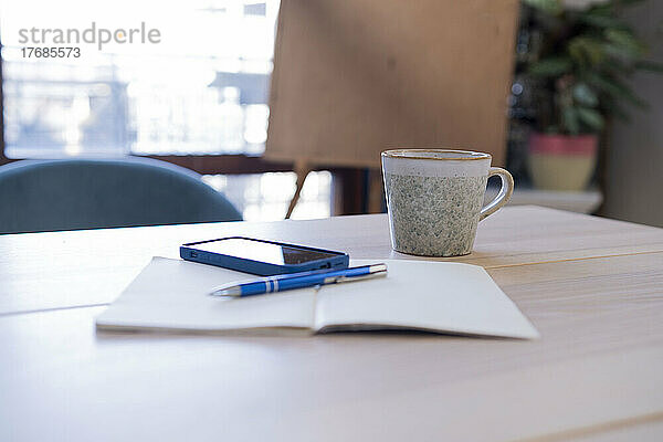 Tagebuch mit Smartphone und Kaffeetasse auf dem heimischen Tisch