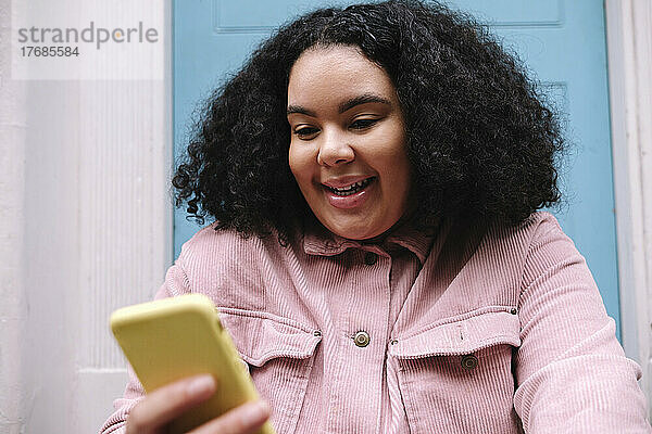 Glückliche junge Frau mit lockigem Haar  die per Smartphone im Netz surft
