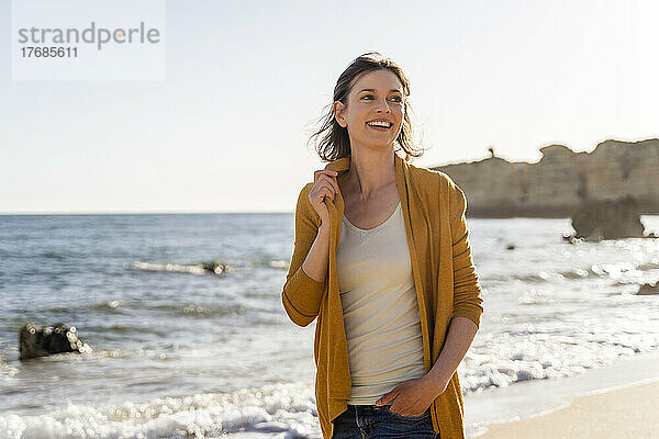 Lächelnde Frau  die an einem sonnigen Tag am Strand steht