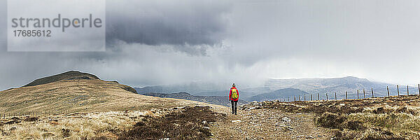 Aktive Seniorin mit Rucksack beim Wandern auf dem Berg unter bewölktem Himmel