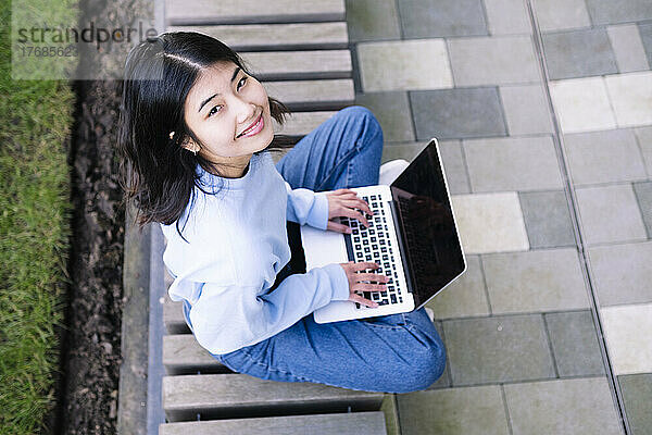 Glückliche junge Frau sitzt mit Laptop auf dem Sitz