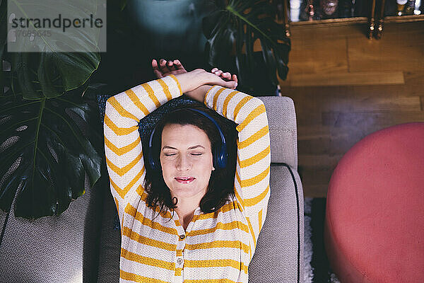 Frau mit Kopfhörern entspannt sich zu Hause auf dem Sofa