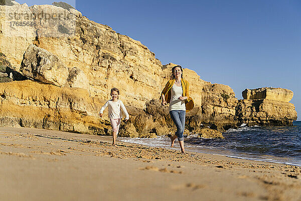 Lächelnde Mutter und Tochter laufen am Strand entlang