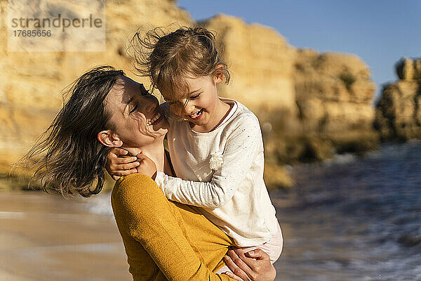 Lächelnde Frau verbringt an einem sonnigen Tag ihre Freizeit mit ihrer Tochter am Strand