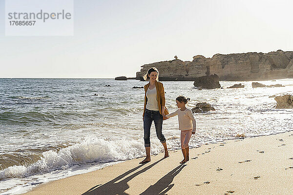 Lächelnde Mutter mit Tochter  die an einem sonnigen Tag am Ufer spaziert