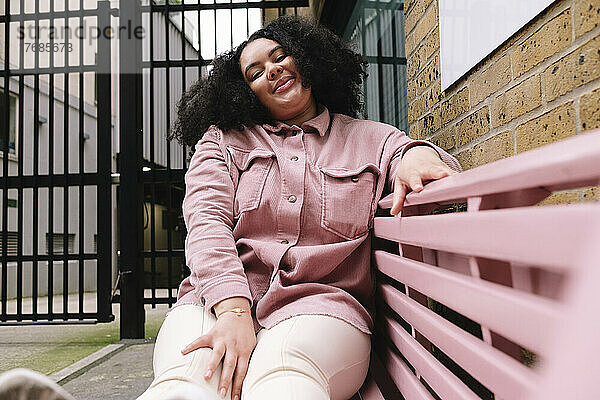 Smiling woman with curly hair sitting on pink bench