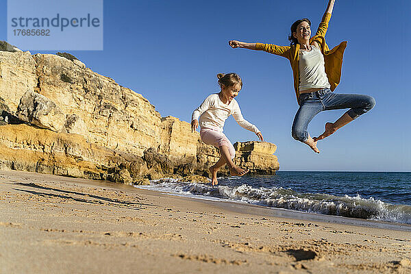 Glückliche Mutter und Tochter springen an einem sonnigen Tag am Strand