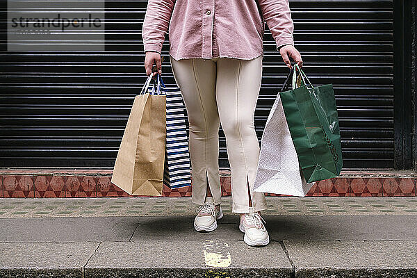 Frau mit Einkaufstüten steht auf Fußweg