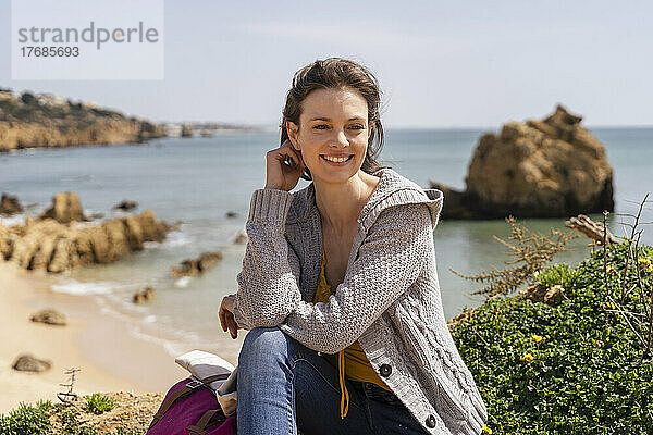 Glückliche Frau  die an einem sonnigen Tag vor dem Meer sitzt