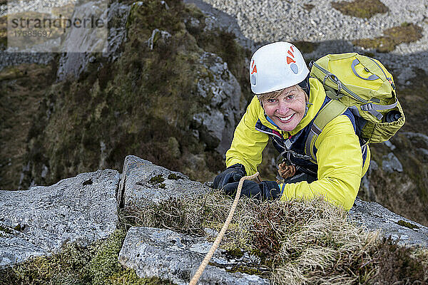 Smiling woman wearing sports helmet climbing rocky mountain