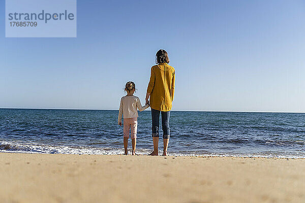 Frau mit Tochter steht am Ufer und blickt auf den Horizont