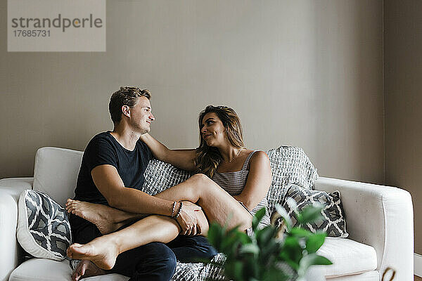 Lächelndes junges Paar  das sich zu Hause auf dem Sofa anschaut