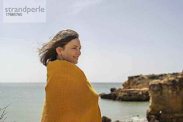 Glückliche Frau  eingewickelt in eine gelbe Decke  genießt den sonnigen Tag