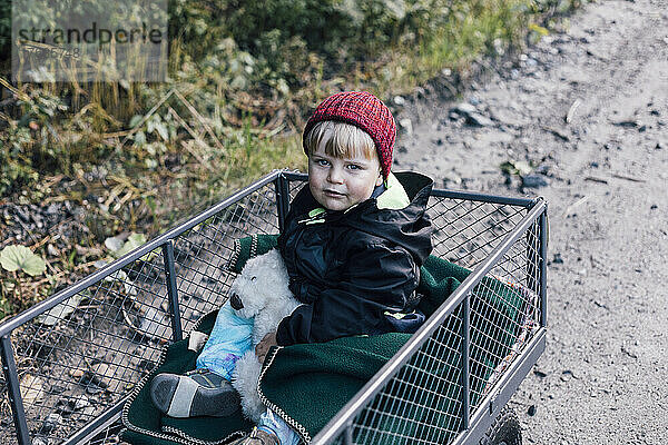 Junge mit Spielzeug sitzt im Gartenwagen
