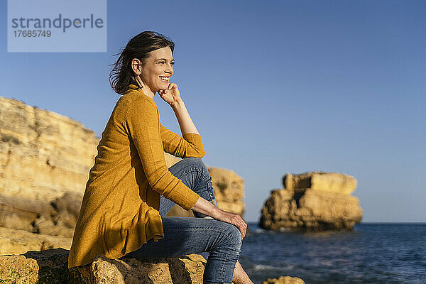 Glückliche Frau sitzt auf einem Felsen am Strand