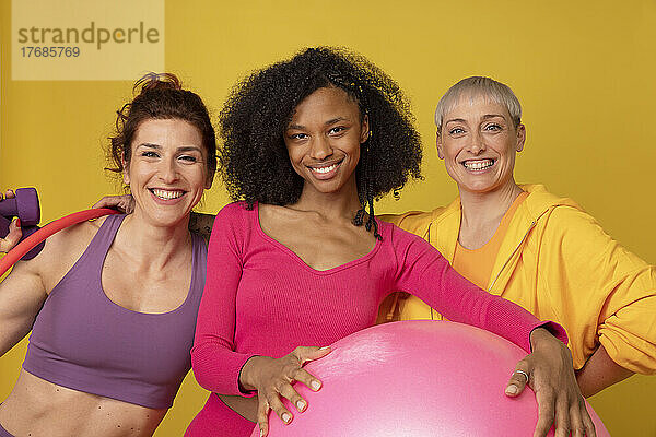 Lächelnde  gemischtrassige Freunde mit Fitnessgeräten vor gelbem Hintergrund