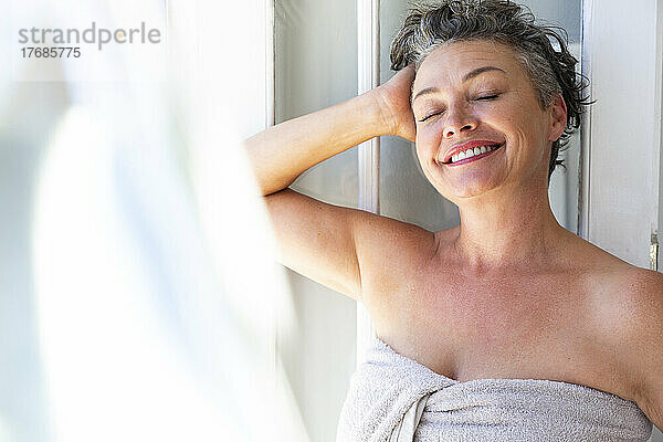 Happy woman with hand in hair standing by window at home