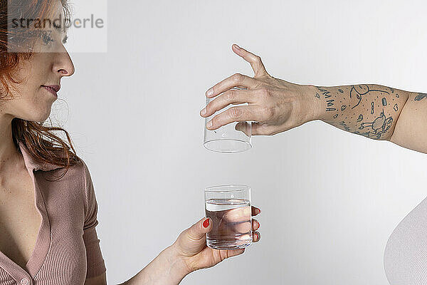 Hände einer Frau füllen Glas mit Wasser vor weißem Hintergrund