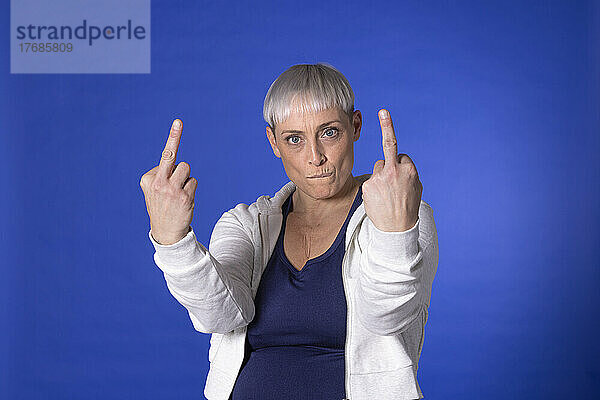 Wütende Frau zeigt obszöne Geste vor blauem Hintergrund
