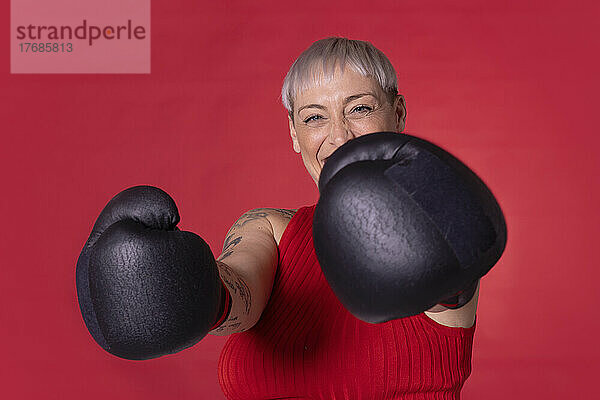 Glückliche Frau mit Boxhandschuhen  die vor rotem Hintergrund steht